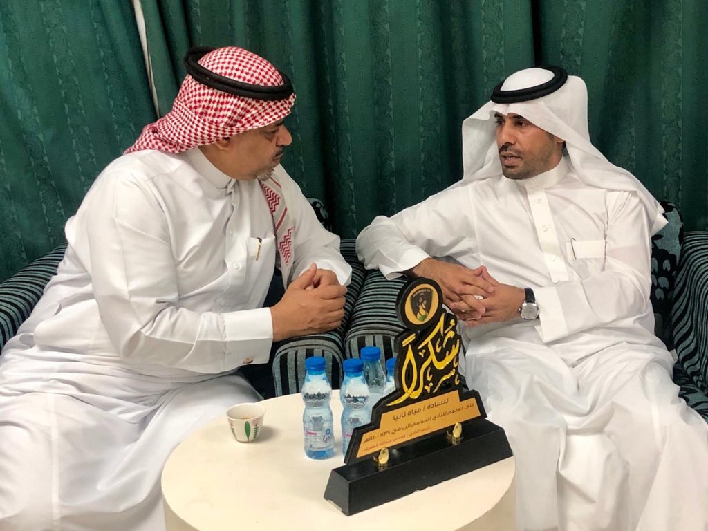 رجلان يجلسان على أريكة، يرتديان الأبيض، مع كأس في المنتصف، يظهران سعادة الإنجاز.